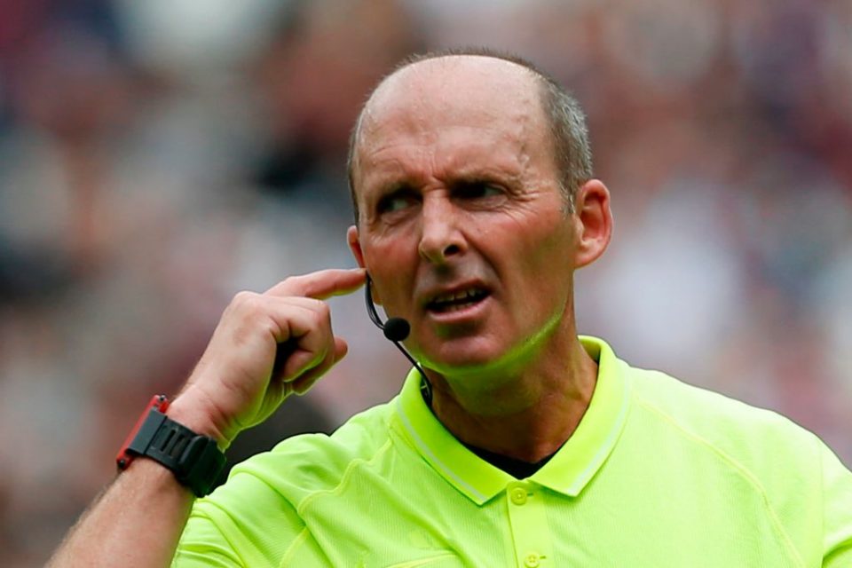 Referee Mike Dean communicates with the VAR (video assistant referee) as a Manchester City penalty, which was saved, is being checked and ruled that it must be retaken during the English Premier League football match between West Ham United and Manchester City at The London Stadium, in east London on August 10, 2019. (Photo by Ian KINGTON / AFP) / RESTRICTED TO EDITORIAL USE. No use with unauthorized audio, video, data, fixture lists, club/league logos or 'live' services. Online in-match use limited to 120 images. An additional 40 images may be used in extra time. No video emulation. Social media in-match use limited to 120 images. An additional 40 images may be used in extra time. No use in betting publications, games or single club/league/player publications. / (Photo credit should read IAN KINGTON/AFP/Getty Images)