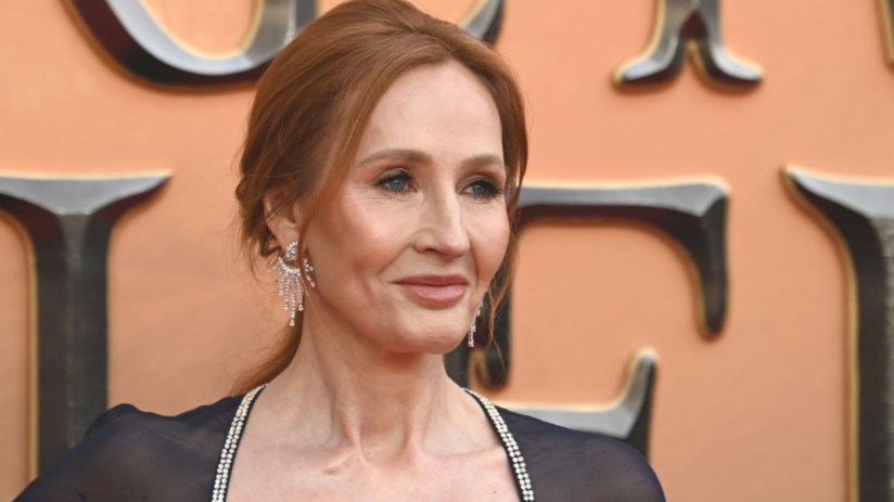 JK Rowling speaking at a public event, wearing a formal outfit, addressing an audience with a focused expression.