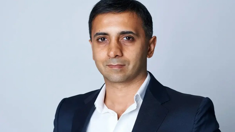 Tej Lalvani smiling during a business conference, wearing a suit and tie, highlighting his role as a prominent entrepreneur