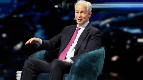 Jamie Dimon speaking at a JP Morgan event, wearing a suit and tie, addressing financial trends and market strategies.