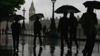 Rainy and gloomy British landscape with overcast skies, wet streets, and people holding umbrellas in a busy city setting.