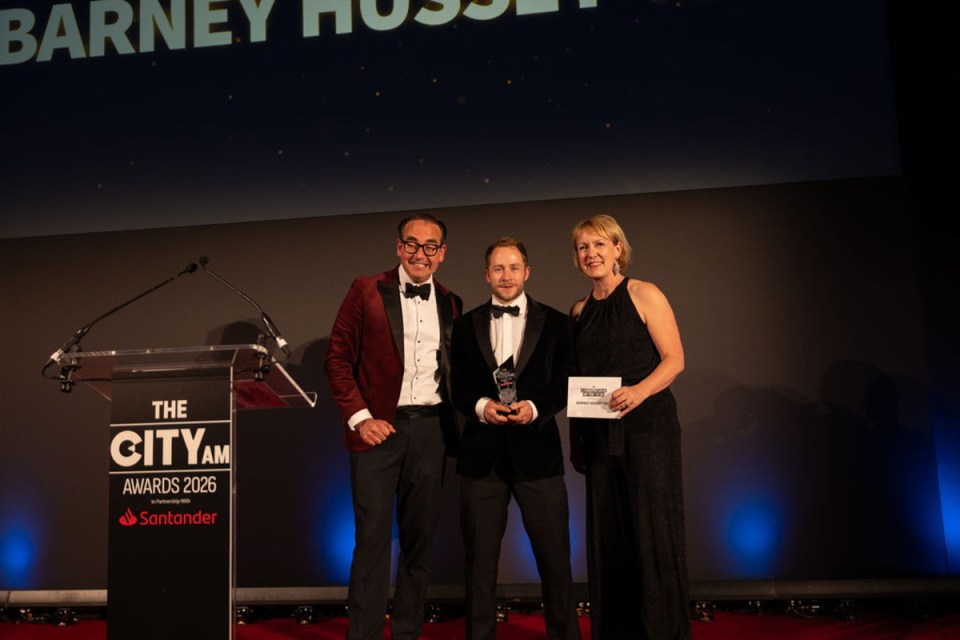 Barney receiving award at City PM Awards ceremony, surrounded by applauding attendees in formal attire