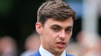 Donnacha OBrien confidently poses at a racetrack, showcasing his professional demeanor and equestrian attire.