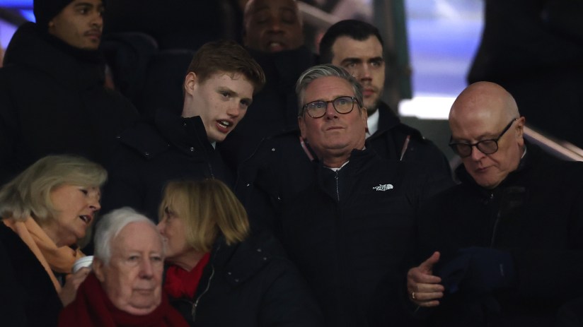 Keir Starmer visits Arsenal football ground, engaging in discussions with fans and officials in a vibrant stadium setting.