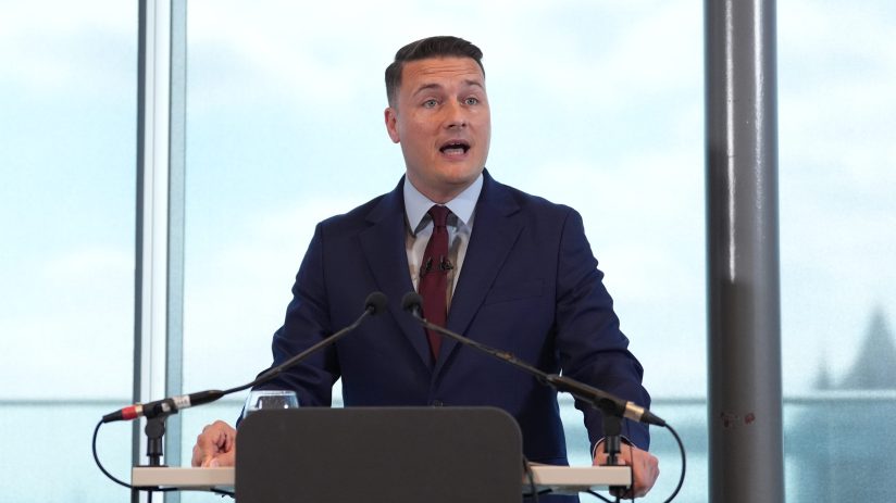 Wes Streeting, British politician, delivering a speech at a press conference with a focused expression and engaging the au...