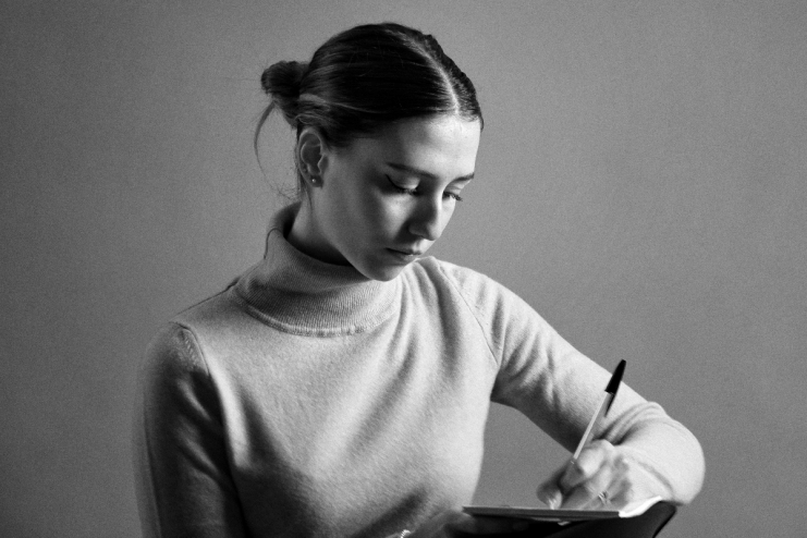 Young woman in turtleneck writing intently with a pen, dark bun hairstyle, black and white image