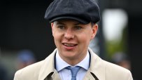 Smiling man in flat cap, light trench coat, white shirt, and blue tie, looking right.