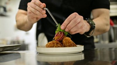 Chef garnishing falafel with microgreens and pickled onions using tweezers on a white plate in a kitchen