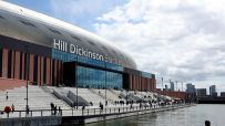 Hill Dickinson Stadium exterior, Liverpool, with fans on steps, waterfront, and city skyline.
