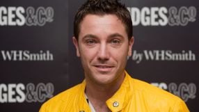 Gino DAcampo, smiling in a bright yellow jacket, against a dark background with GES & CO and WHSmith logos
