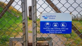 Southern Water safety sign on a chain link fence, detailing required PPE like hard hats and safety boots.