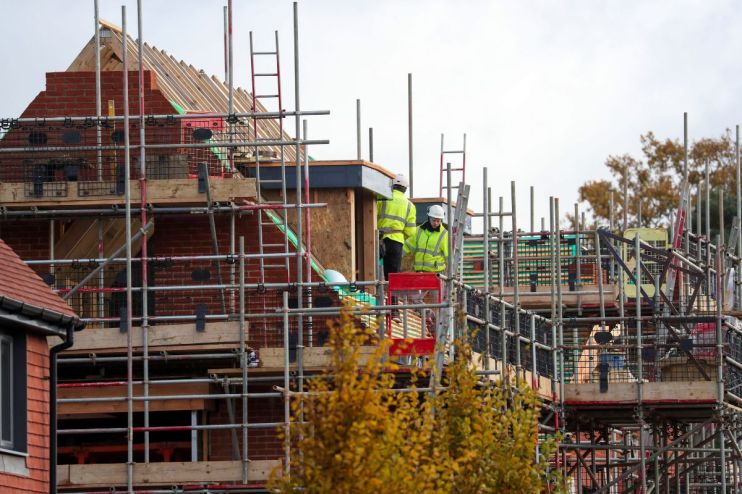 Construction workers in hard hats and high-vis jackets on scaffolding around a Vistry housing development.