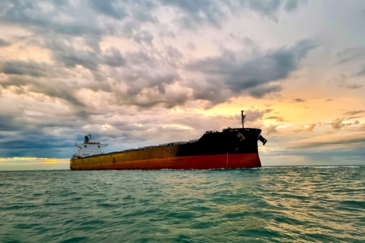 Large oil tanker navigating a strait under a cloudy sky, impacting oil prices and global trade.
