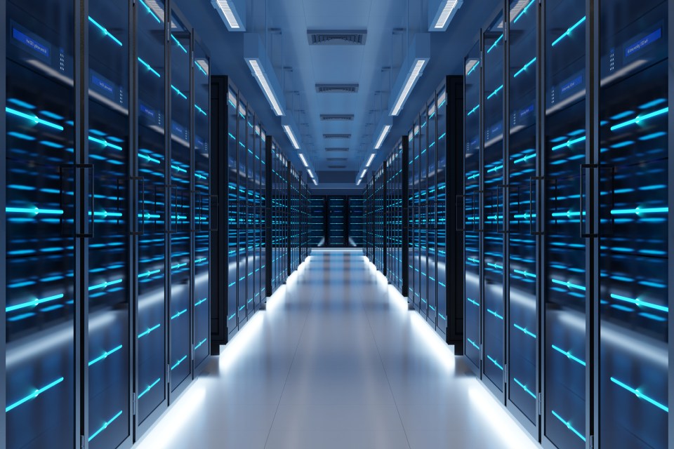 Long hallway in a modern data center with rows of black server racks glowing with blue lights.