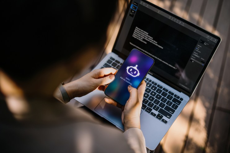 A person interacting with a chatbot on a smartphone, with a laptop in the background, showcasing AI and technology.