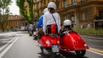Tourists on a red Vespa with sidecar ride through Rome, Italy, past historic buildings.