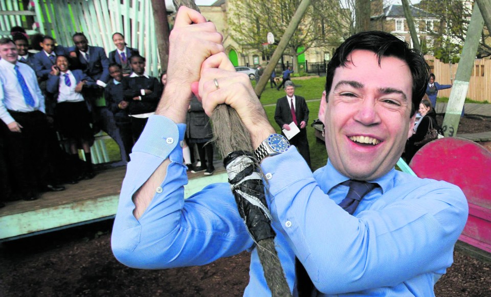 Andy Burnham smiling, holding a rope on a playground with schoolchildren and adults in the background.
