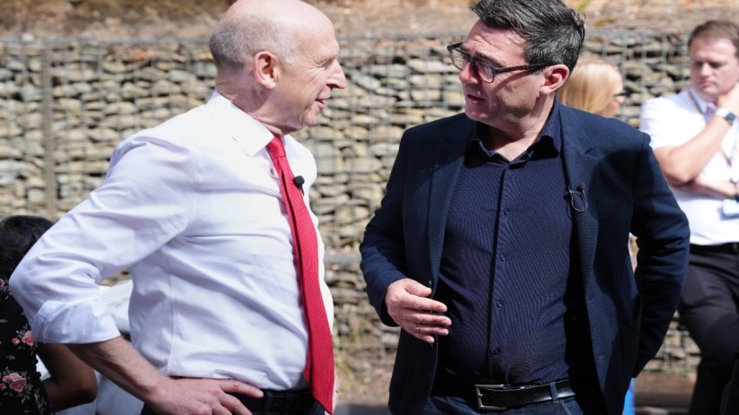 Two men, one in a white shirt and red tie, the other in a navy jacket, conversing outdoors.