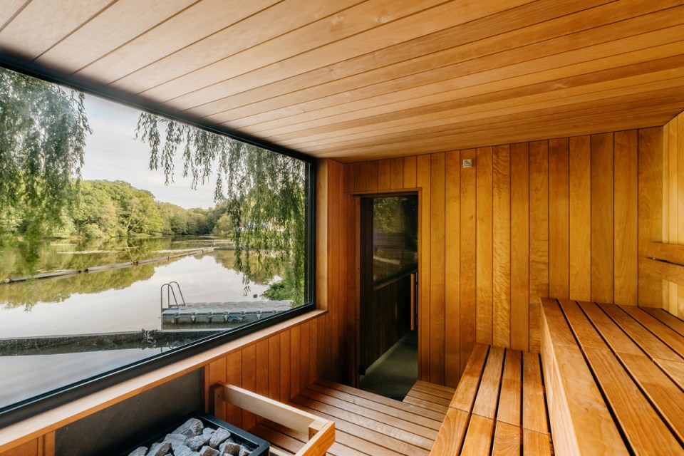 Modern wood sauna interior with large window overlooking a serene lake and trees.