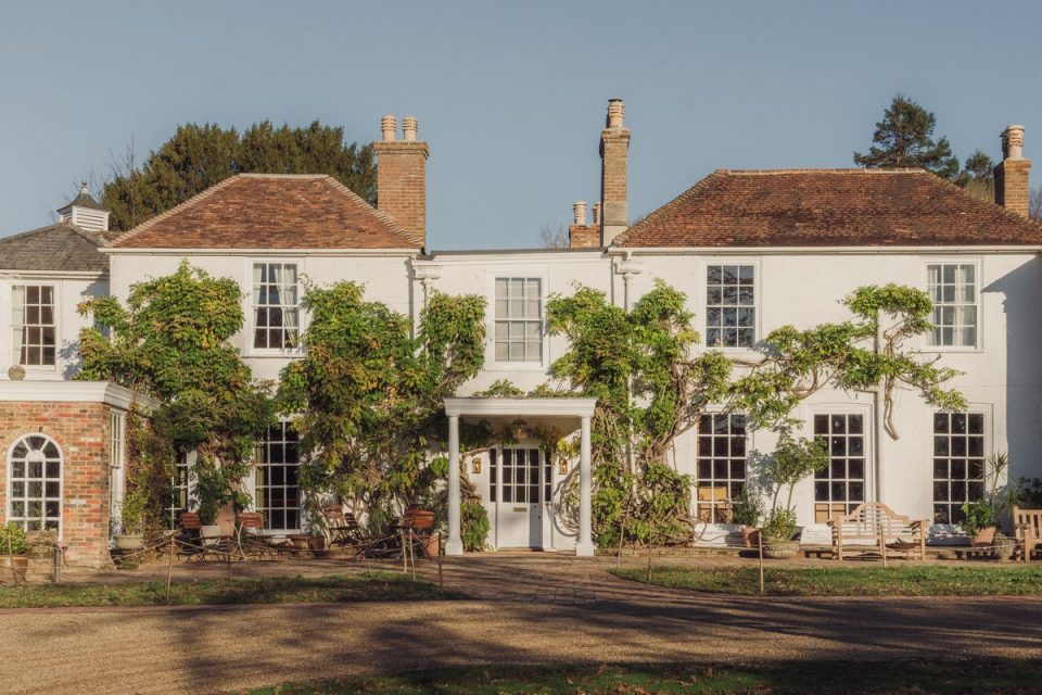 Crafted exterior of a large white house with green vines, multiple windows, and a gravel driveway.