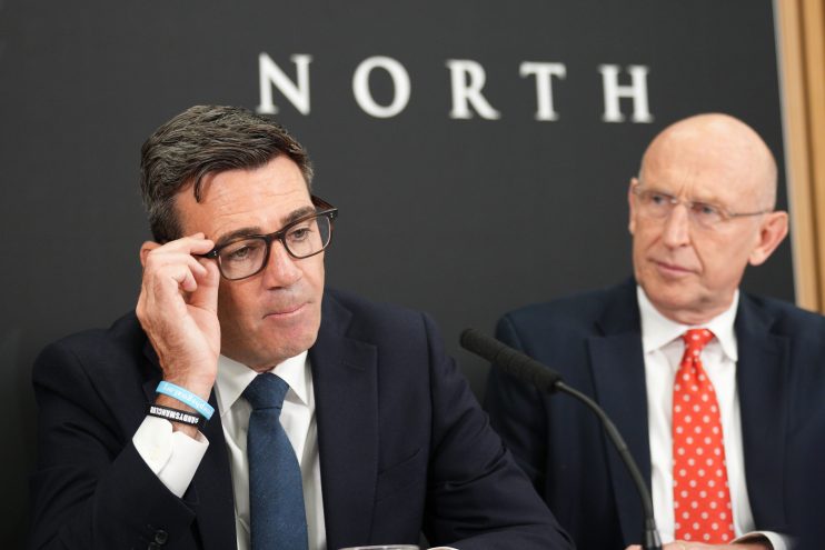 Andy Burnham and John Healey at Number 10 North, both wearing suits and ties, with a microphone in the foreground.