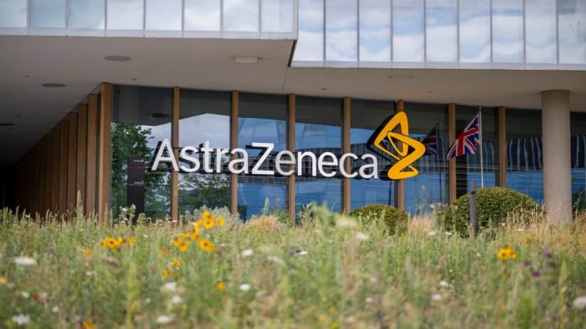 AstraZeneca building exterior with logo, glass facade, UK flag, and wildflowers in foreground.