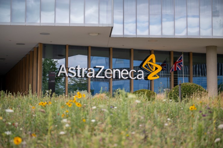 AstraZeneca building exterior with logo, glass facade, UK flag, and wildflowers in foreground.