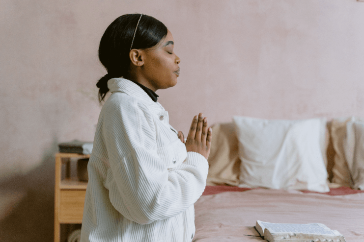 Woman with closed eyes praying over an open Book of Common Prayer on a bed