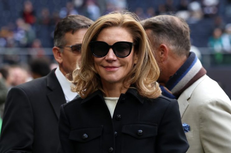 Smiling woman with blonde hair and black sunglasses in a black coat