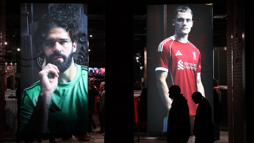 Large display screens featuring Liverpool FC players Alisson Becker and Harvey Elliott in a retail store window.
