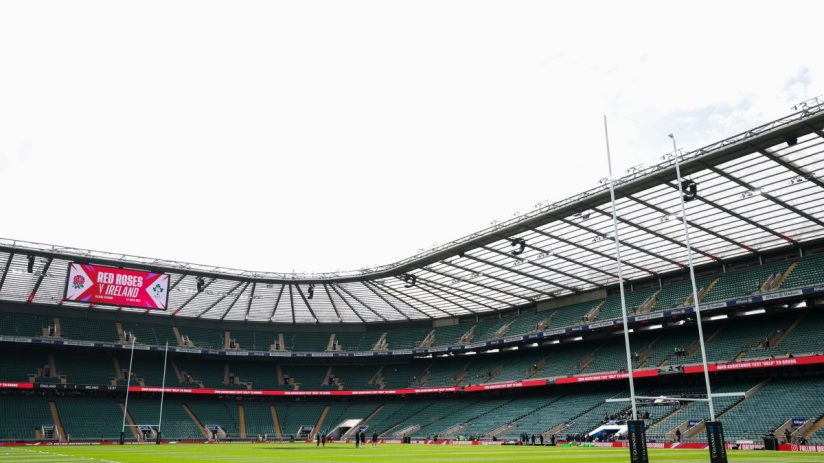 Rugby stadium interior with large screen displaying Red Roses v Ireland, goalposts, and empty green seats