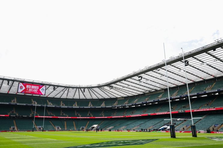 Rugby stadium interior with large screen displaying Red Roses v Ireland, goalposts, and empty green seats