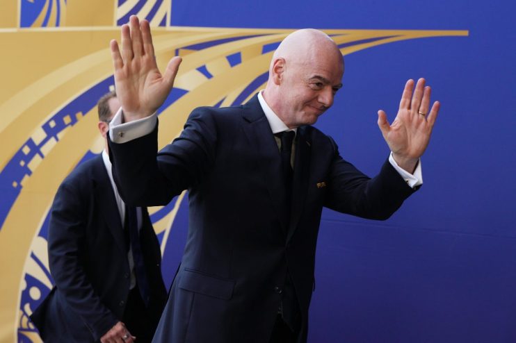 Gianni Infantino, FIFA President, waves to a crowd with a blue and gold patterned background