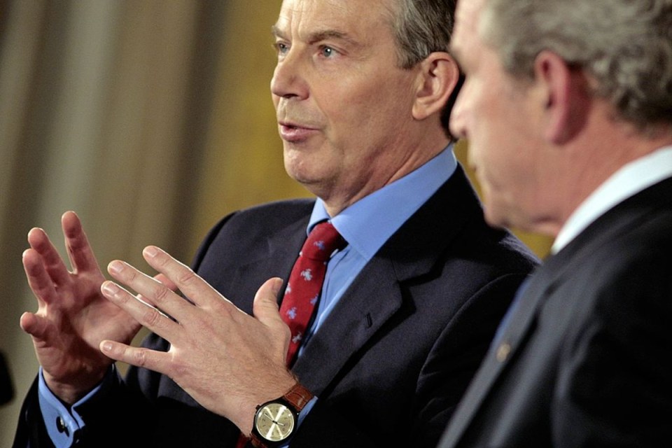 Tony Blair speaking, gesturing with hands, next to George W. Bush; both men in suits and ties.