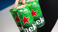 Hand holding a 4-pack of green Heineken beer cans with red stars and white lettering