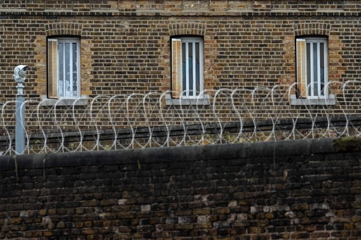 Brick prison wall with barred windows, razor wire, and a security camera.