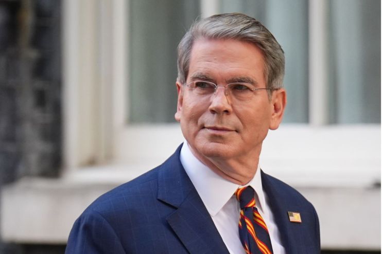 Scott Bessent, a man with gray hair and glasses, wearing a blue suit and striped tie, looking to the side.