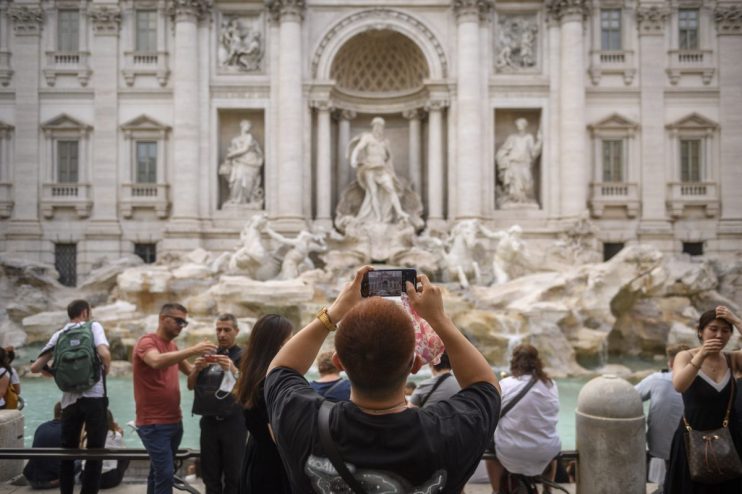 Tourists photograph the ornate white marble Trevi Fountain in Rome, Italy.