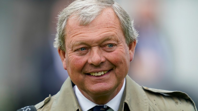 William Haggas, a man with gray hair and blue eyes, smiling and wearing a tan coat and patterned tie