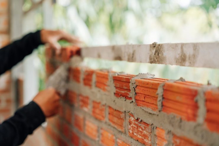 Construction workers hands building a brick wall with mortar and a leveling tool, demonstrating masonry work