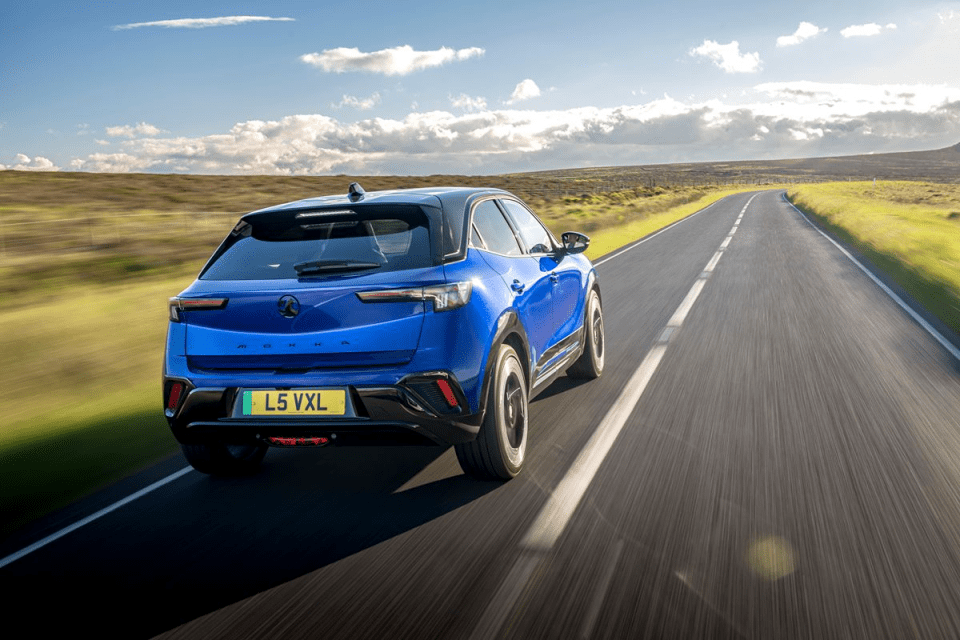 Blue Vauxhall Mokka driving on a rural road with motion blur, sun shining on the landscape.