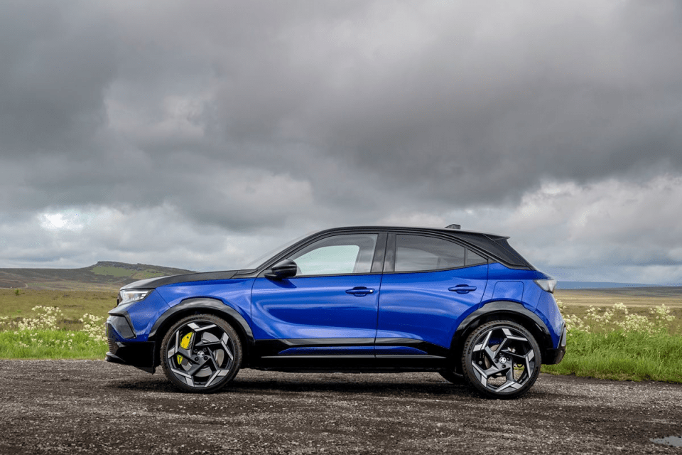 Blue and black compact SUV on a gravel road with a cloudy sky and green hills in the background.